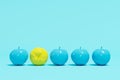 Outstanding yellow apple among blue apples on pastel blue background