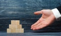 The outstretched hand of a businessman points to a pyramid of wooden squares. Concept promoter, sale and purchase of goods.