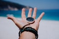 Outstretched hand holding black metal compass against white sandy beach and blue sea. Find your way or goal concept