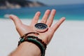 Outstretched hand holding black metal compass against white sandy beach and blue sea. Find your way or goal concept