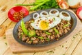 Oval bowl of meat, omelet, onion circles, pepper and some vegetables nearby