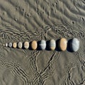 Oval pebbles in varying sizes, arranged linearly on textured sand. Sand displays rippled patterns, Royalty Free Stock Photo
