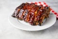 Oven-baked barbecue ribs with sauce on a white plate with a red checkered picnic napkin