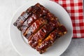 Oven-baked barbecue ribs with sauce on a white plate with a red checkered picnic napkin