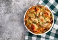 Oven Baked Chicken and Rice with onions, carrots and herbs in a white baking dish on a dark grey background