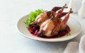 Oven baked quails served with berry sauce on stone plate close up