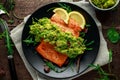 Oven cooked salmon steak, fillet with avocado salsa and green on black plate. wooden table. healthy food