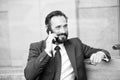 Over the phone. Portrait of modern businessman talking on smart-phone while sitting on bench outdoors. bearded man holding glasses Royalty Free Stock Photo