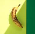 Over ripe banana with dark spots on hard light with shadows, yellow background with green border