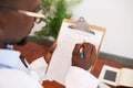 Over the shoulder shot of doctor filling in patient symptom checklist clipboard