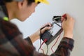 Over shoulder view of electrician installer using a multimeter to test power line current in electrical system