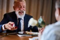 Over shoulder view of mature man in tuxedo proposing to woman holding white rose in restaurant Royalty Free Stock Photo