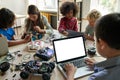 Diverse schoolkids at stem class building robot using pc with white screen.