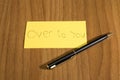 Over to you handwrite on a yellow paper with a pen on a teble