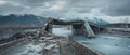 Overcast sky looms over the ruins of a demolished bridge, with a mountain backdrop and frigid river running beneath.