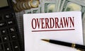 OVERDRAWN - word on a white sheet on the background of a calculator, coins and dollar bills Royalty Free Stock Photo