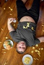 overeat fat boy eat junk food while lying on floor at home, with french fries