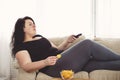 Overweight woman with tv remote and junk food Royalty Free Stock Photo