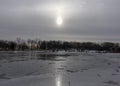 Overexposed sun behind deciduous trees in winter reflecting into the ice sheet of a river Royalty Free Stock Photo