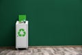 Overfilled trash bin with recycling symbol near color wall indoors