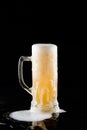 Overflowing mug of fresh cold light beer with froth flowing on the table and beautiful spilled beer on a black background with Royalty Free Stock Photo