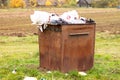 Overflowing rusty trash can in the countryside. Rubbish scattered on the ground, environmental protection problem