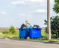 Overflowing waste cans with garbage bags, cardboard boxes and other garbage near the road. One waste can is broken Royalty Free Stock Photo