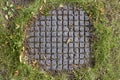 Overgrown with green grass old sewer manhole with a checkered pattern. rough surface texture Royalty Free Stock Photo