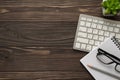 Overhead above flatlay view photo of computer keyboard eyewear plant notebook and eyewear isolated brown wooden backdrop