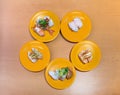 Overhead angle photography of an assortment of nigiri-zushi or sushi on five yellow plates arranged in circle on the table.