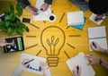 Overhead of business team with yellow wood panel and lightbulb graphic