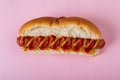 Overhead close-up of mustered sauce and tomato sauce on hot dog over pink background