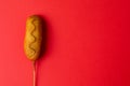 Overhead close-up shot of corn dog with mustered sauce over skewer on red background with copy space