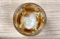 Overhead close up view of a glass of whiskey drink with round ice cube on table