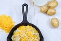 Overhead, flat lay photo. Half of a cast iron skillet filled with sliced potatoes and onions with grated cheese and bread crumbs o