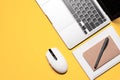 Overhead flat lay photo with a silver grey laptop computer, wireless plastic mouse, notebooks, and a pen on a vivid yellow Royalty Free Stock Photo