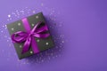 Overhead photo of black giftbox with ribbon wrapped as bow and confetti around isolated on the violet background Royalty Free Stock Photo