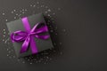 Overhead photo of black giftbox with violet ribbon wrapped as bow confetti and glitter around isolated on the black background Royalty Free Stock Photo