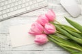 Overhead photo of bouquet of pink tulips lying on wooden desktop with white keyboard computer mouse and paper card with copy space Royalty Free Stock Photo
