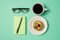 Overhead photo of cup of coffee notepad with pen glasses and plate with fruit cake isolated on the teal backdrop Royalty Free Stock Photo