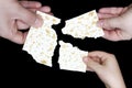 An overhead photo of Jewish child, woman and men hands hold matza, leavened bread isolated on black background. Hands holding matz