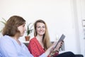 Two beautiful young women at home sitting on sofa while using a tablet PC computer and smiling Royalty Free Stock Photo