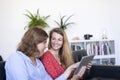 Two beautiful young women at home sitting on sofa while using a tablet PC computer and smiling Royalty Free Stock Photo