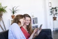 Two beautiful young women at home sitting on sofa while using a tablet PC computer and smiling Royalty Free Stock Photo