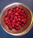 Overhead picture of bowl of raspberries in gold bowl with blue background