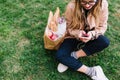 Overhead portrait of young woman in striped pants sitting on lawn after shopping and writing message. Cute girl in Royalty Free Stock Photo