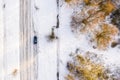 Overhead shot of a car driving on an isolated snowy road next to yellow trees Royalty Free Stock Photo