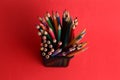 Overhead shot of colorful pencils in a metal pen holder on a red background Royalty Free Stock Photo