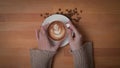 Overhead shot of female hands holding a cup of latte coffee on wooden Royalty Free Stock Photo