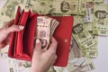 Overhead shot of female hands opening a red wallet with money on top of a heap of colorful pesos